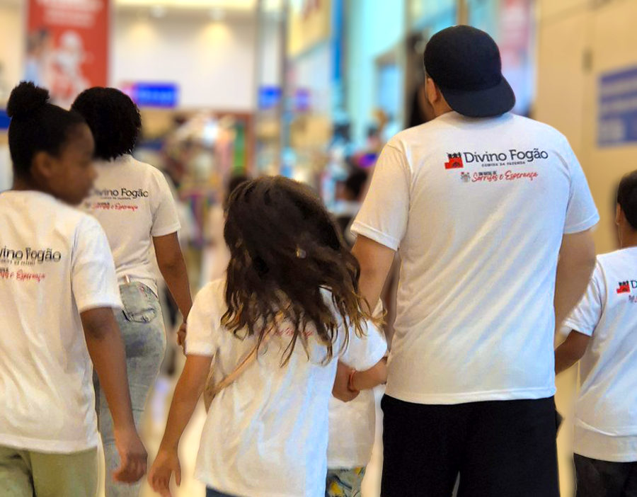 Crianças e voluntários com camisetas do Divino Fogão passeando no shopping no Natal Feliz